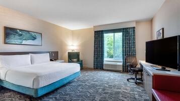 A hotel room with a bed, a desk with a TV, a chair, a lamp, and a window with curtains.