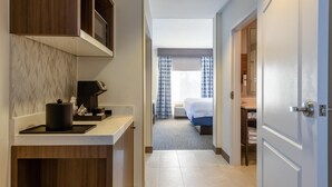 A hotel hallway with a kitchen area on the left, a bed with blue curtains in the center, and a bathroom visible through an open door on the right. - Hilton Garden Inn Auburn Lewiston Riverwatch (Auburn)