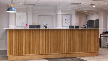 Una mesa de recepción con detalles de madera, una lámpara colgante azul y un quiosco digital.