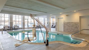 Piscina interna con poltrona elevatrice, pareti piastrellate e vista sull'esterno.