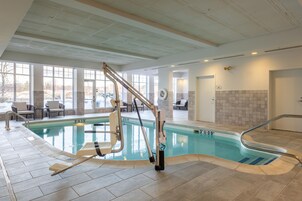Una piscina interior con un elevador de sillas, paredes enlosadas y vistas al exterior.