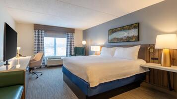 Een hotelkamer met een groot bed, een bureau met stoel, een televisie en een schilderij aan de muur.
