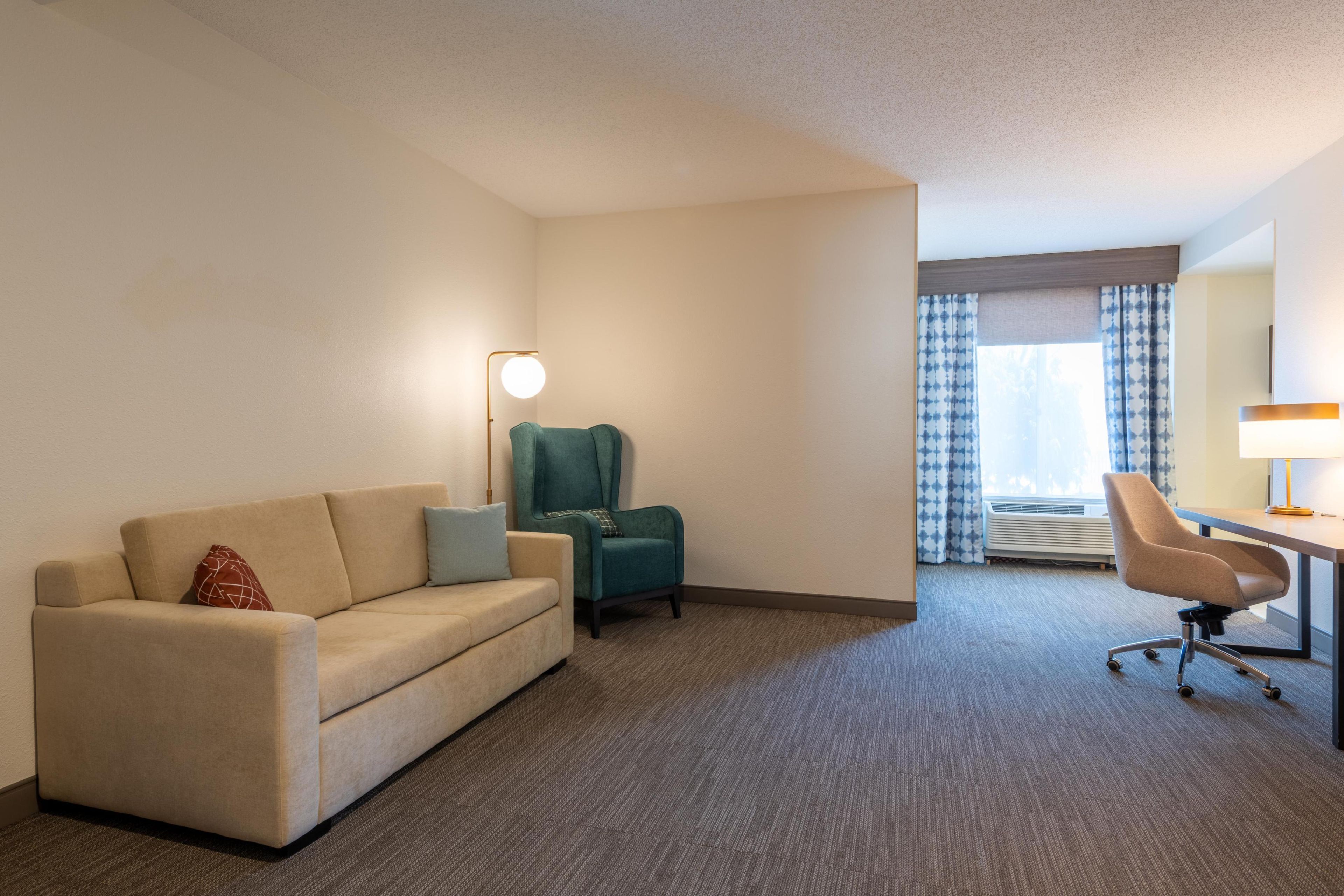 Una habitación de hotel con sofá, una silla, escritorio y lámpara.