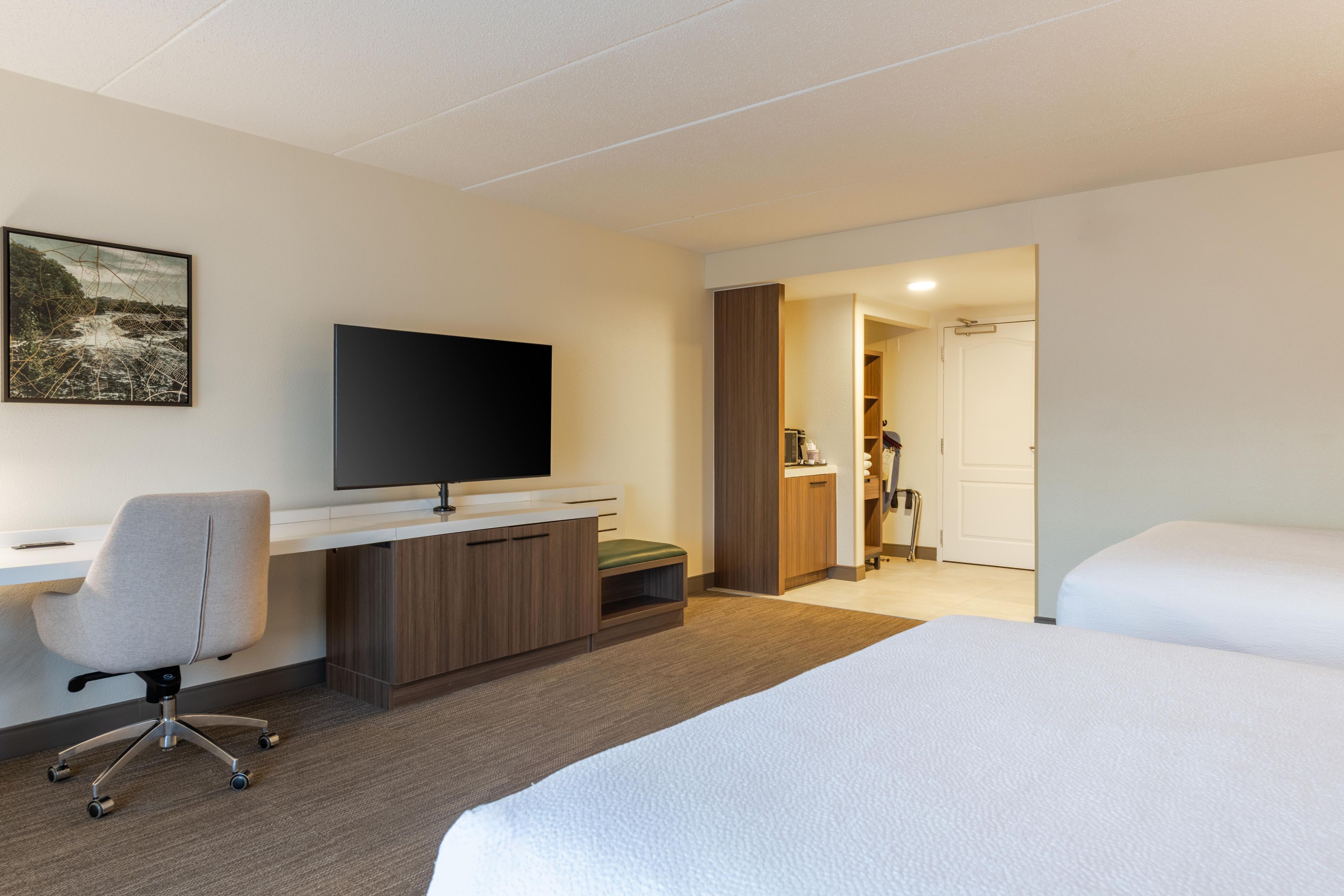 A hotel room with a bed, a desk with a chair, a television, and a bathroom visible through an open door.