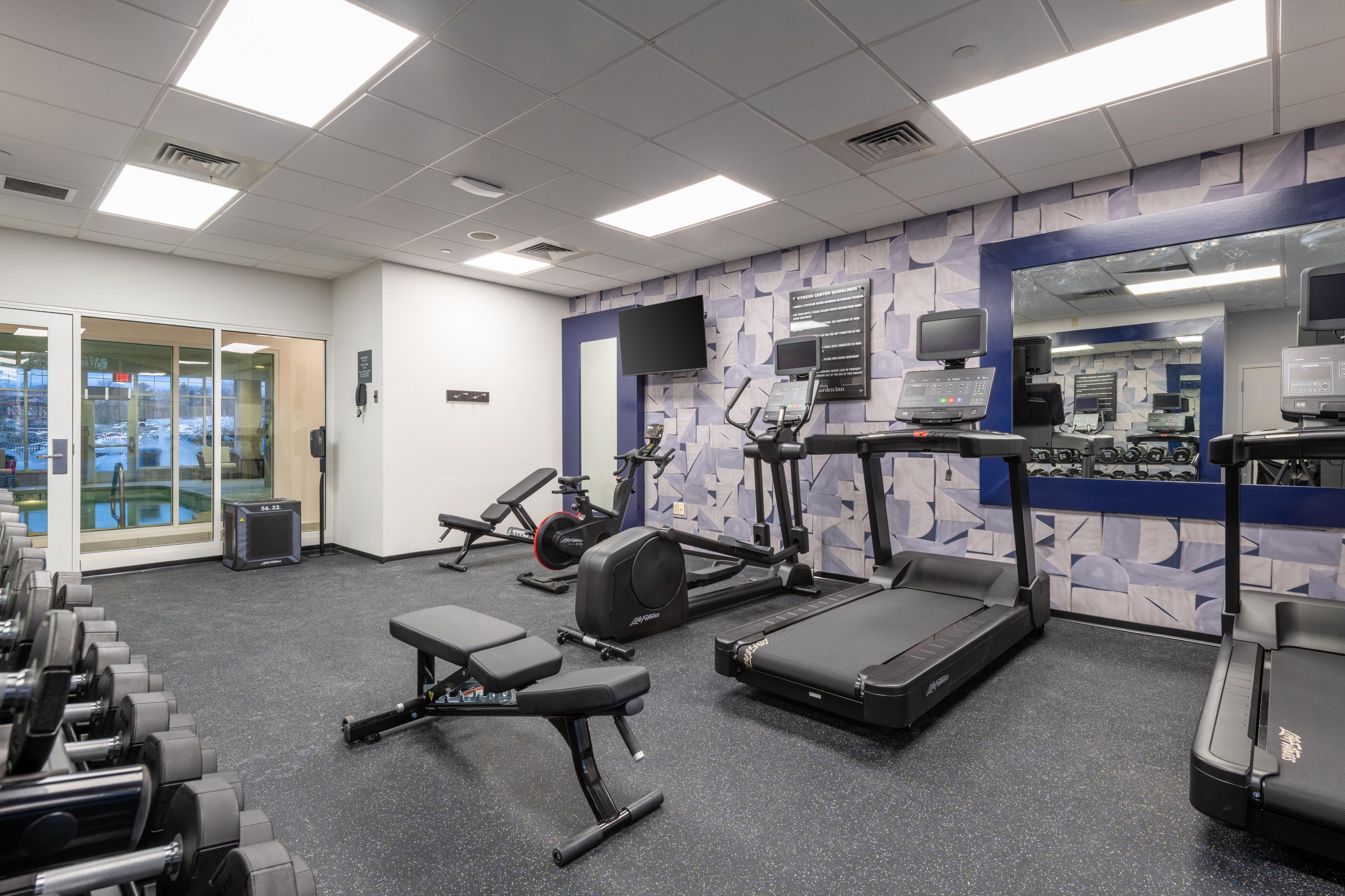 A gym with treadmills, weight machines, and a mirror wall.