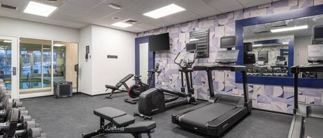 Un gimnasio con cintas de correr, máquinas de pesas y un muro de espejos.
