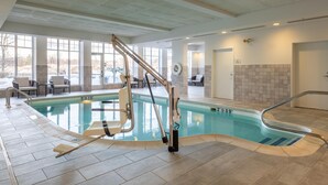 An indoor swimming pool with a lift chair, tiled walls, and a view of the outside. - Hilton Garden Inn Auburn Lewiston Riverwatch (Auburn)