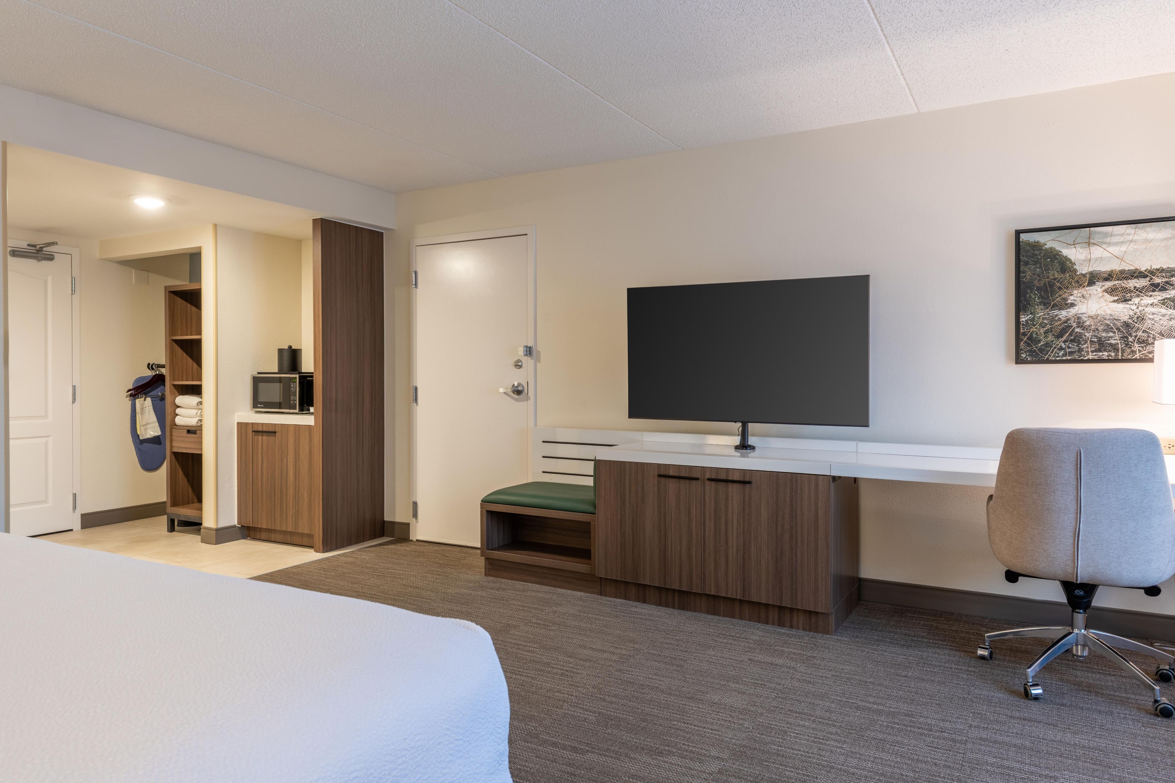 A hotel room with a bed, a desk with a flat-screen TV, a microwave, and a chair.