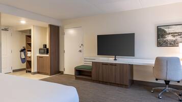 A hotel room with a bed, a desk with a flat-screen TV, a microwave, and a chair.