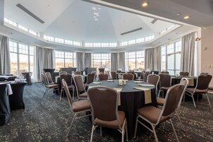 Une salle de conférence équipée de tables rondes, de chaises et d’une grande fenêtre offrant une vue sur l’extérieur.