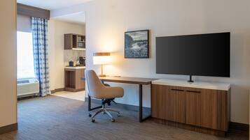 A hotel room with a desk, chair, TV, and kitchenette.