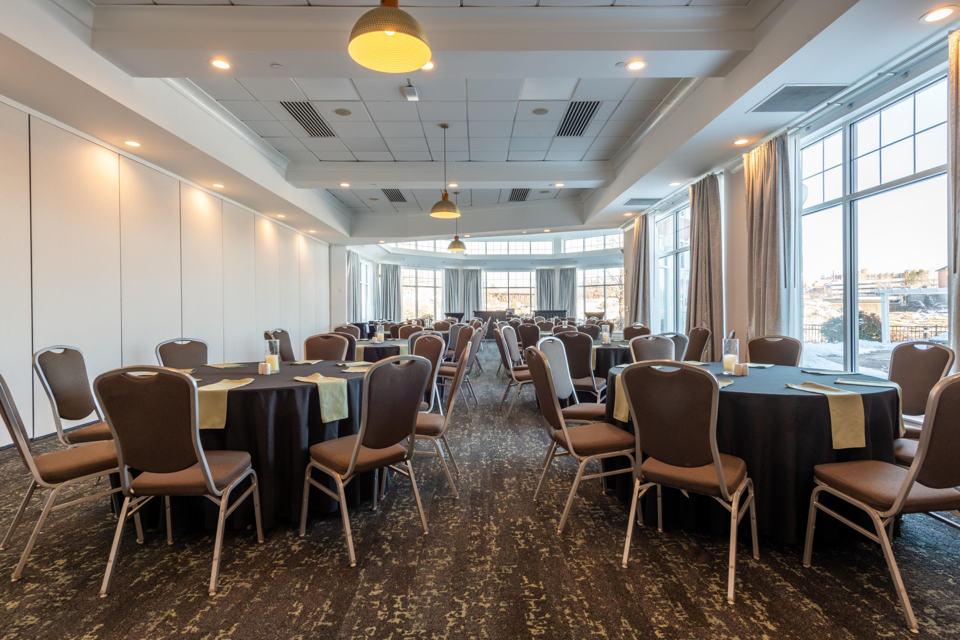 Une salle de conférence dotée de plusieurs tables et chaises, de grandes fenêtres et d’un éclairage au plafond.