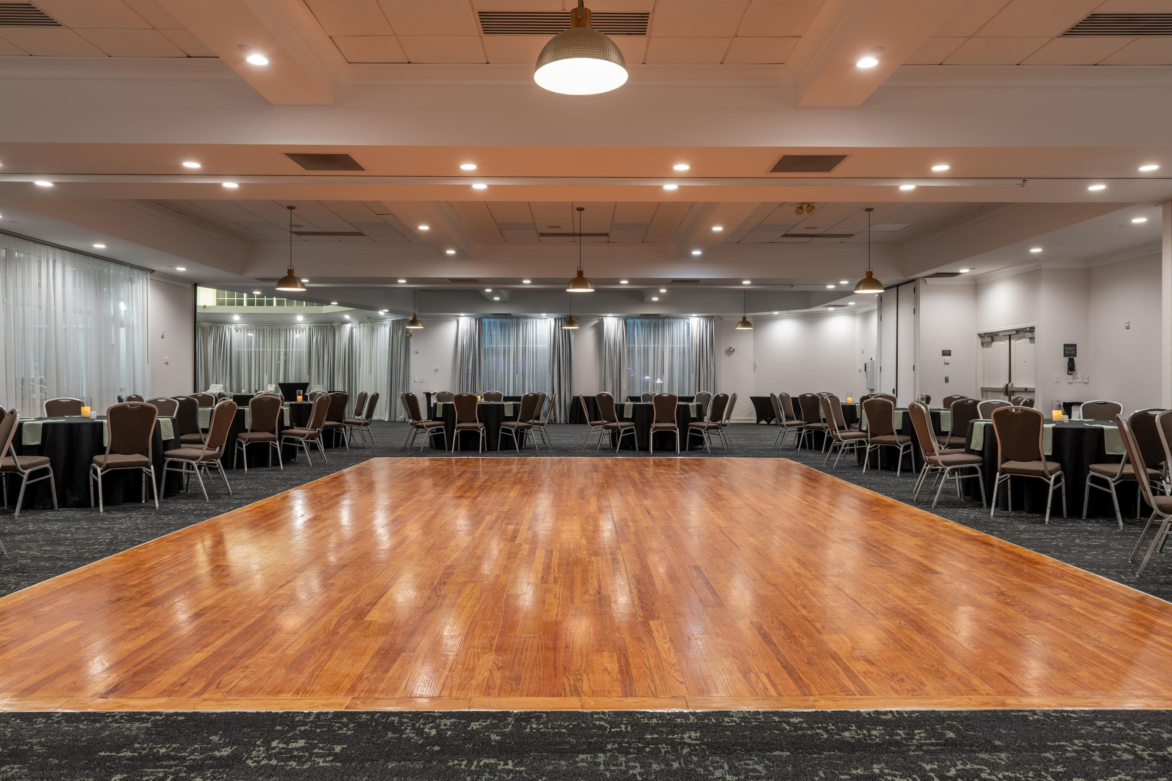 Een vergaderzaal met een grote houten tafel, rijen stoelen en plafondlampen.