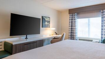A hotel room with a large bed, a desk with a flat-screen TV, a chair, and a window with curtains.