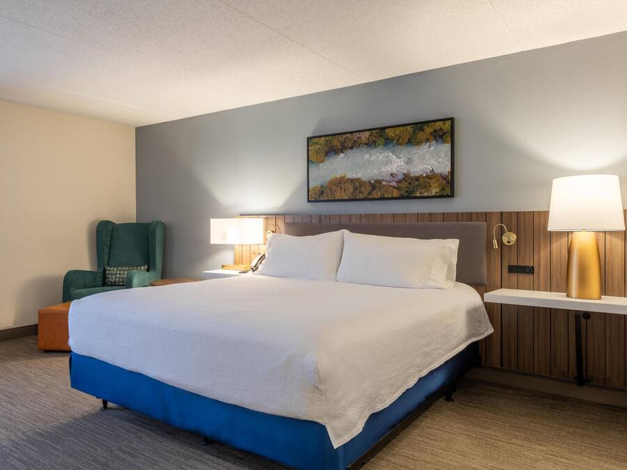 Ein Hotelzimmer mit einem großen Bett, einem Sessel, einem Schreibtisch und einem Bild an der Wand.