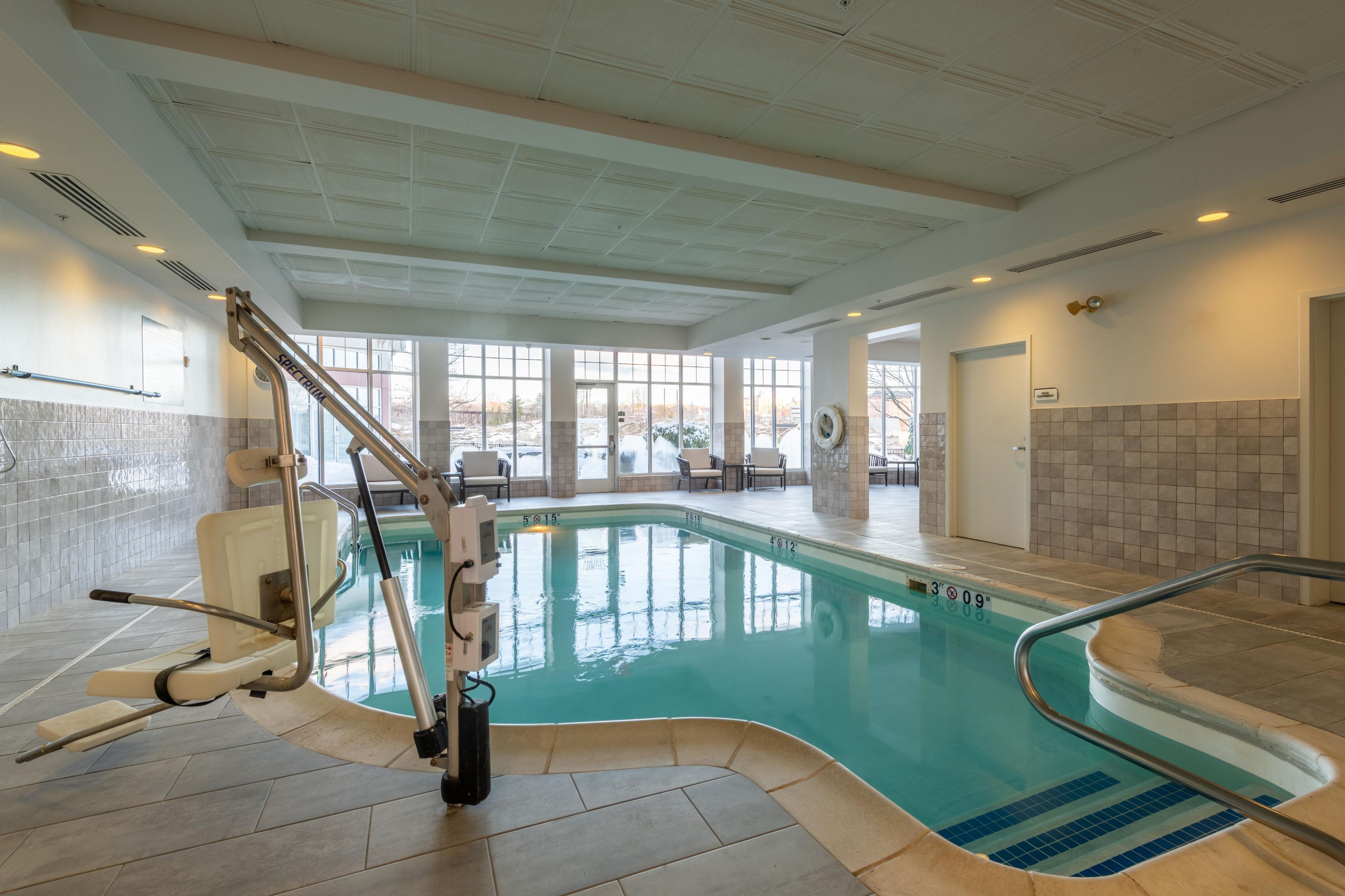 An indoor swimming pool with a sunroof, a changing room, and a seating area with chairs.