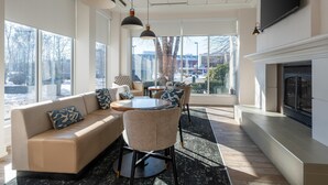 A modern living room with a sofa, chairs, a coffee table, and a fireplace. - Hilton Garden Inn Auburn Lewiston Riverwatch (Auburn)