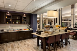 Una cocina moderna con armarios oscuros, una isla central con taburetes altos y una lámpara colgante grande.