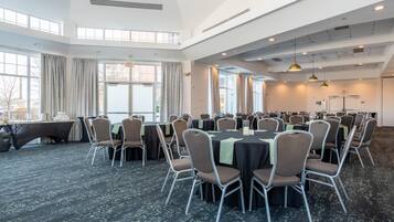 Un salón de conferencias con varias mesas y sillas, ventanas amplias y un techo alto con ventilación.