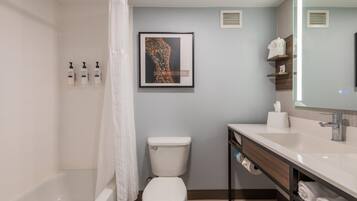 A modern bathroom with a bathtub, toilet, and sink. There are toiletries on the wall and a framed picture above the sink.