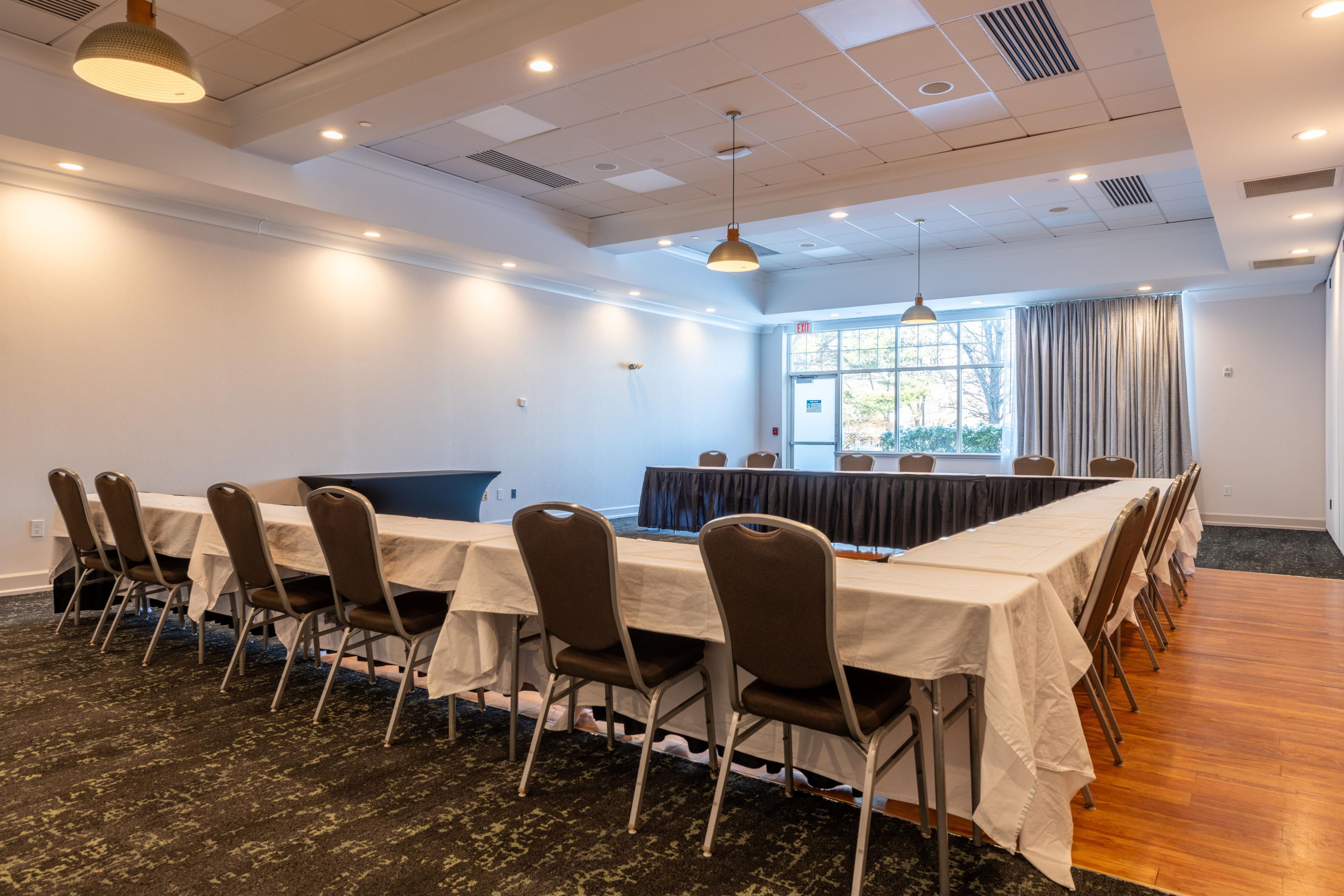 Une salle de conférence avec une longue table, des chaises et une grande fenêtre avec des rideaux.