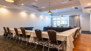 Une salle de conférence avec une longue table, des chaises et une grande fenêtre avec des rideaux.