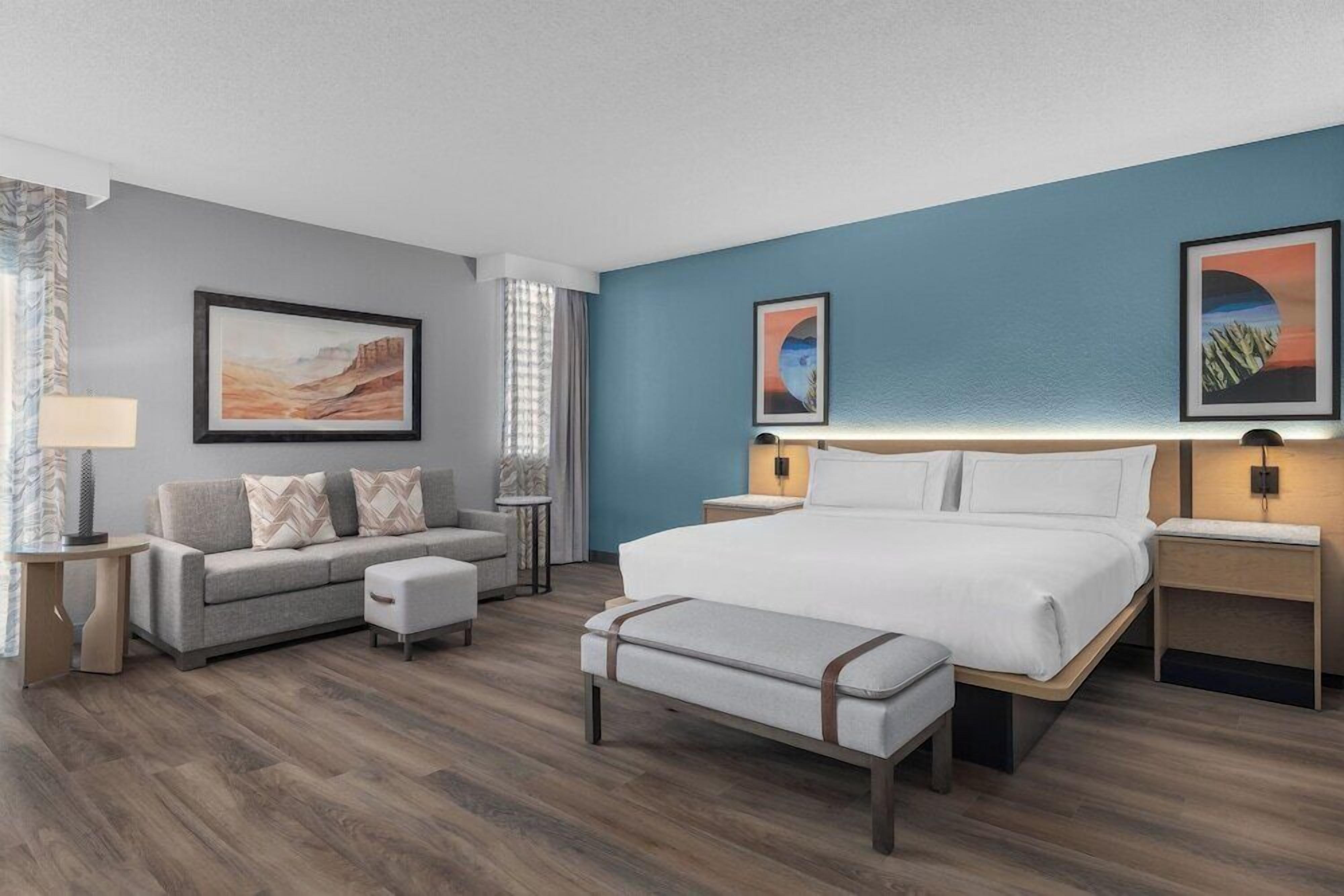 Une chambre d’hôtel comprenant un lit, un canapé, une banquette et deux tables de chevet avec des lampes.