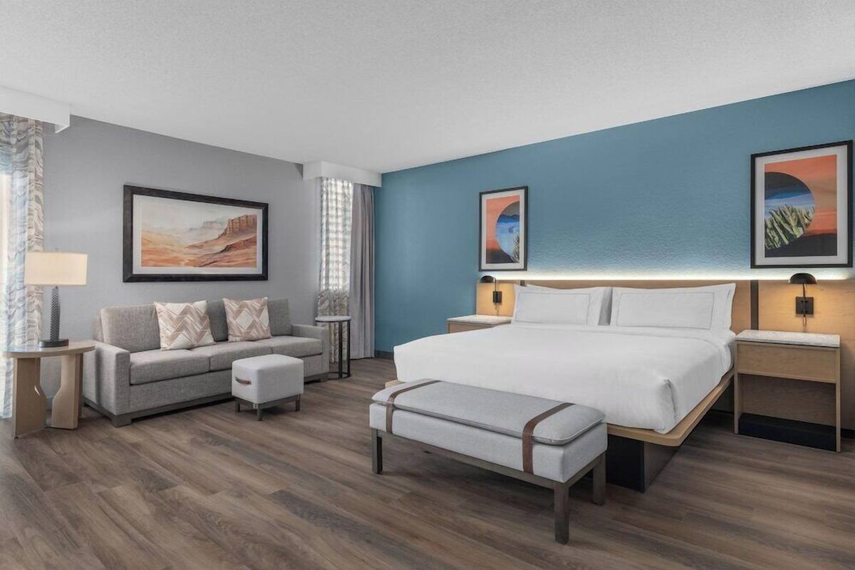 A hotel room with a bed, a sofa, a bench, and two nightstands with lamps.