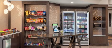 Una estación autoservicio de aperitivos y bebidas con un sistema de pedidos digital, enfriadores para bebidas y un microondas.