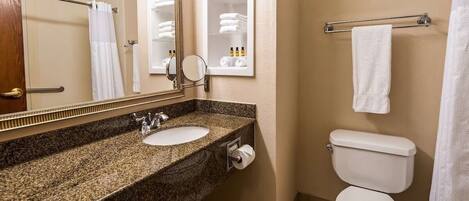 A bathroom with a granite countertop sink, a mirror, a toilet, and a towel rack.