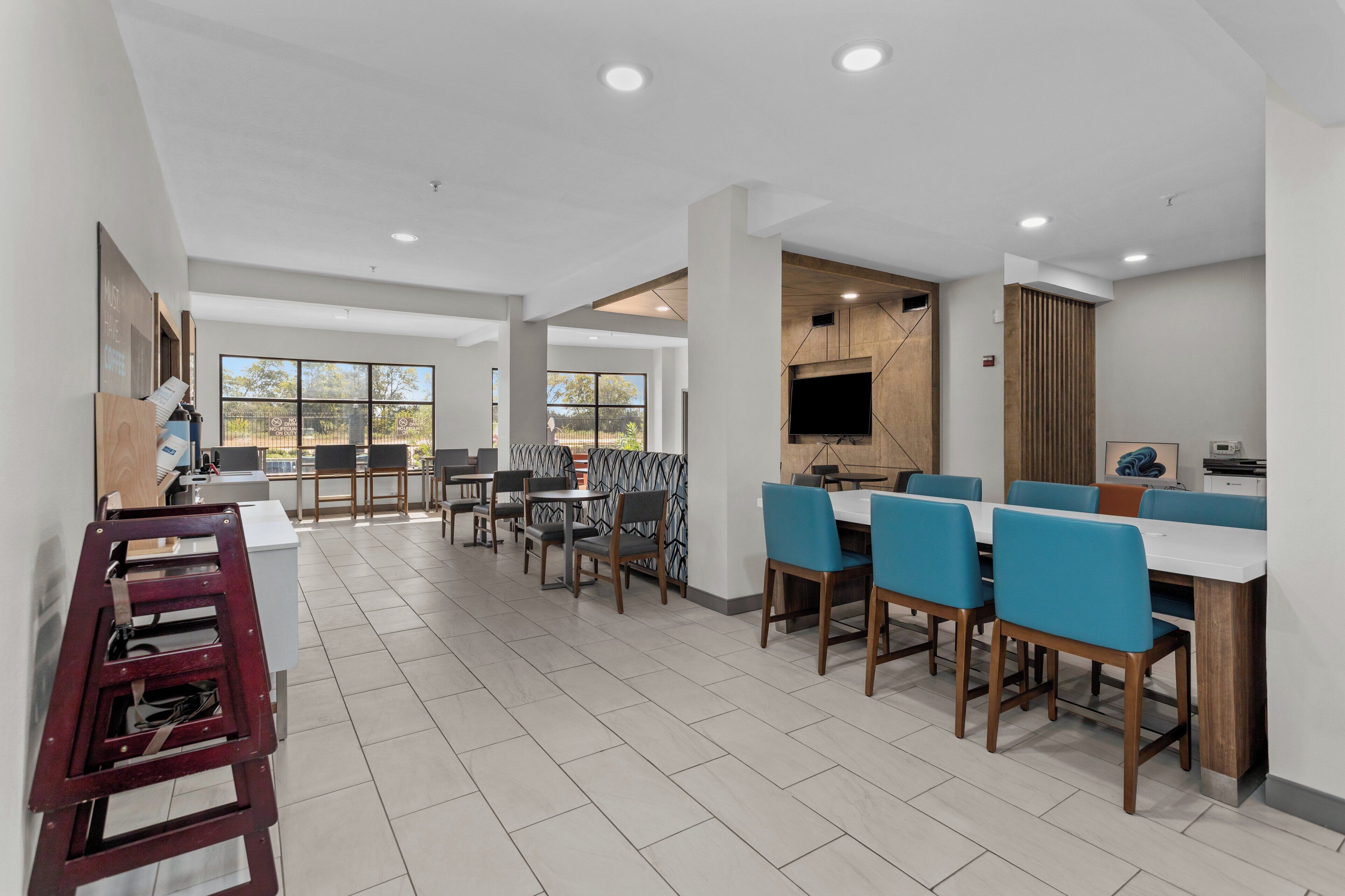 A modern dining area with multiple tables and chairs, a wooden accent wall, and a large window providing a view of the outdoors.