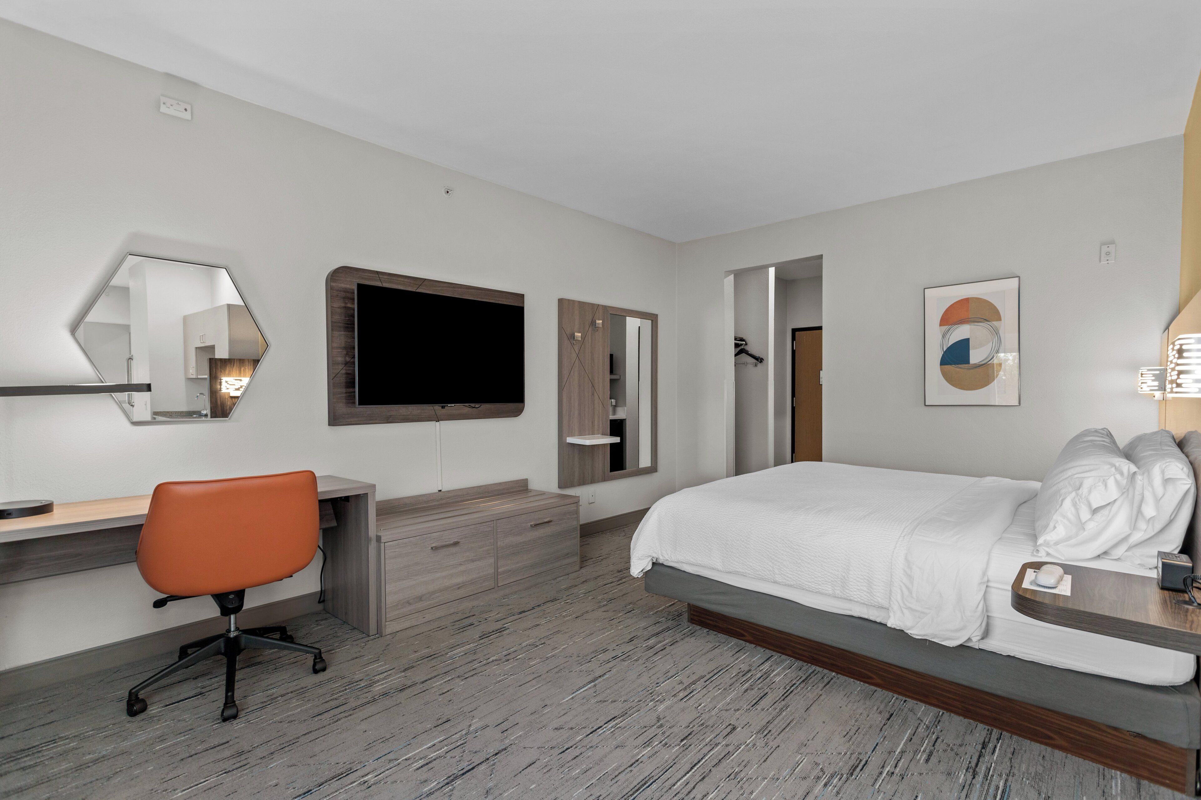 Una habitación de hotel con cama, escritorio, silla, espejo, televisor y armario.