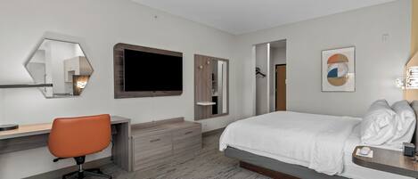 Una habitación de hotel con cama, escritorio, silla, espejo, televisor y armario.