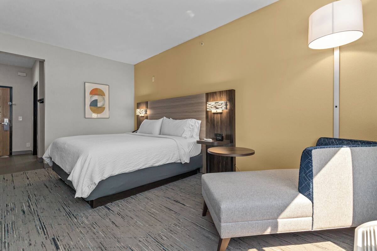 Une chambre d’hôtel moderne avec un grand lit, une petite table ronde, une chaise et une lampe fixée au mur.