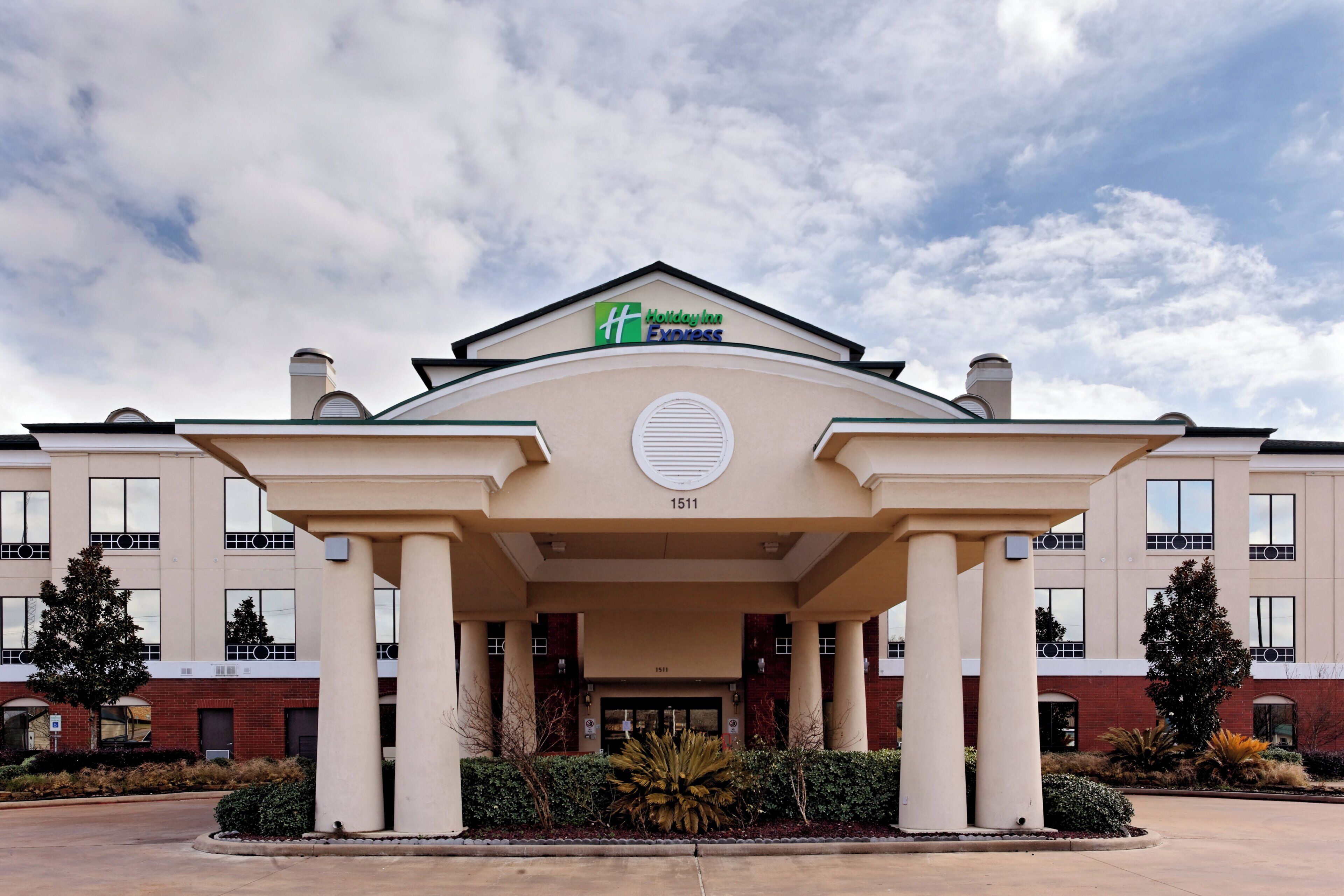 Edificio de Holiday Inn Express con un diseño arquitectónico clásico, que presenta una entrada central con columnas y un amplio ventanal circular encima.