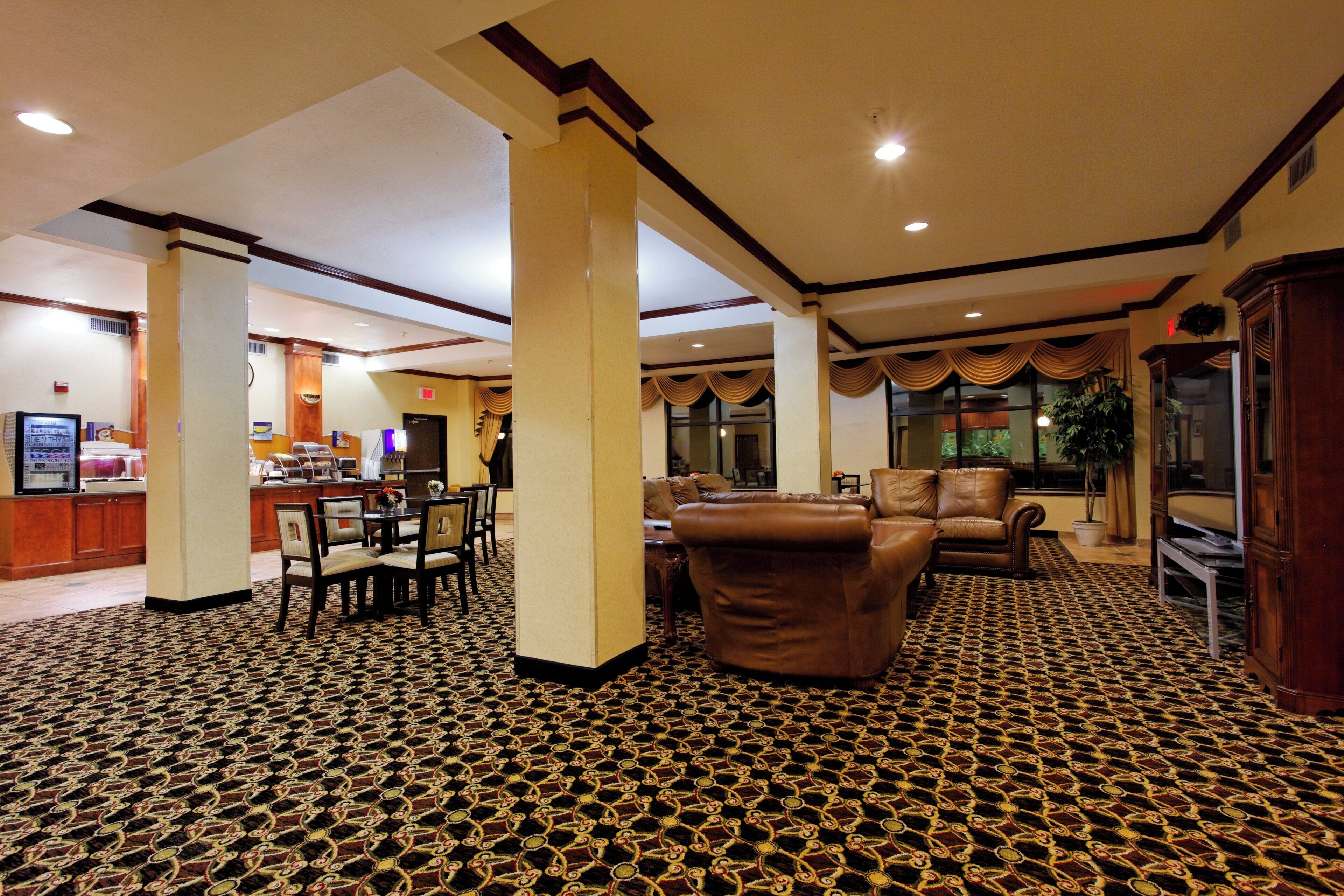 A hotel lobby with a patterned carpet, a reception desk, a dining area, and a seating area with leather sofas.