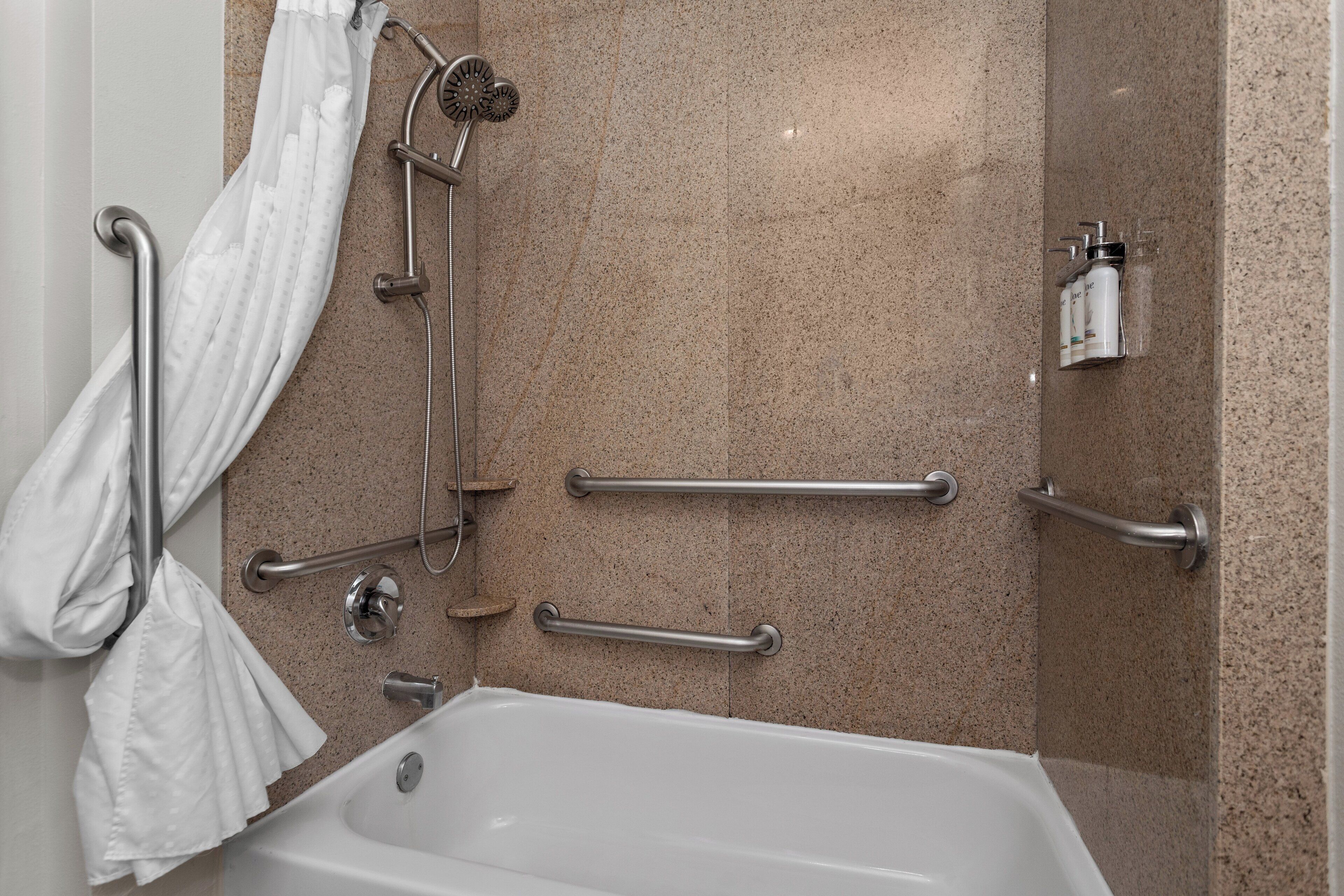 Un baño moderno con bañera, barras de apoyo, cabezal de ducha y perchero.