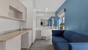 A modern kitchen with white cabinets and a grey countertop, a blue sofa, and a view of the outside through a window. - Holiday Inn Express Crockett by IHG (Crockett)