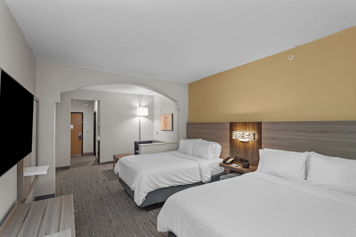 A hotel room with two beds, a TV, a desk, and a lamp.