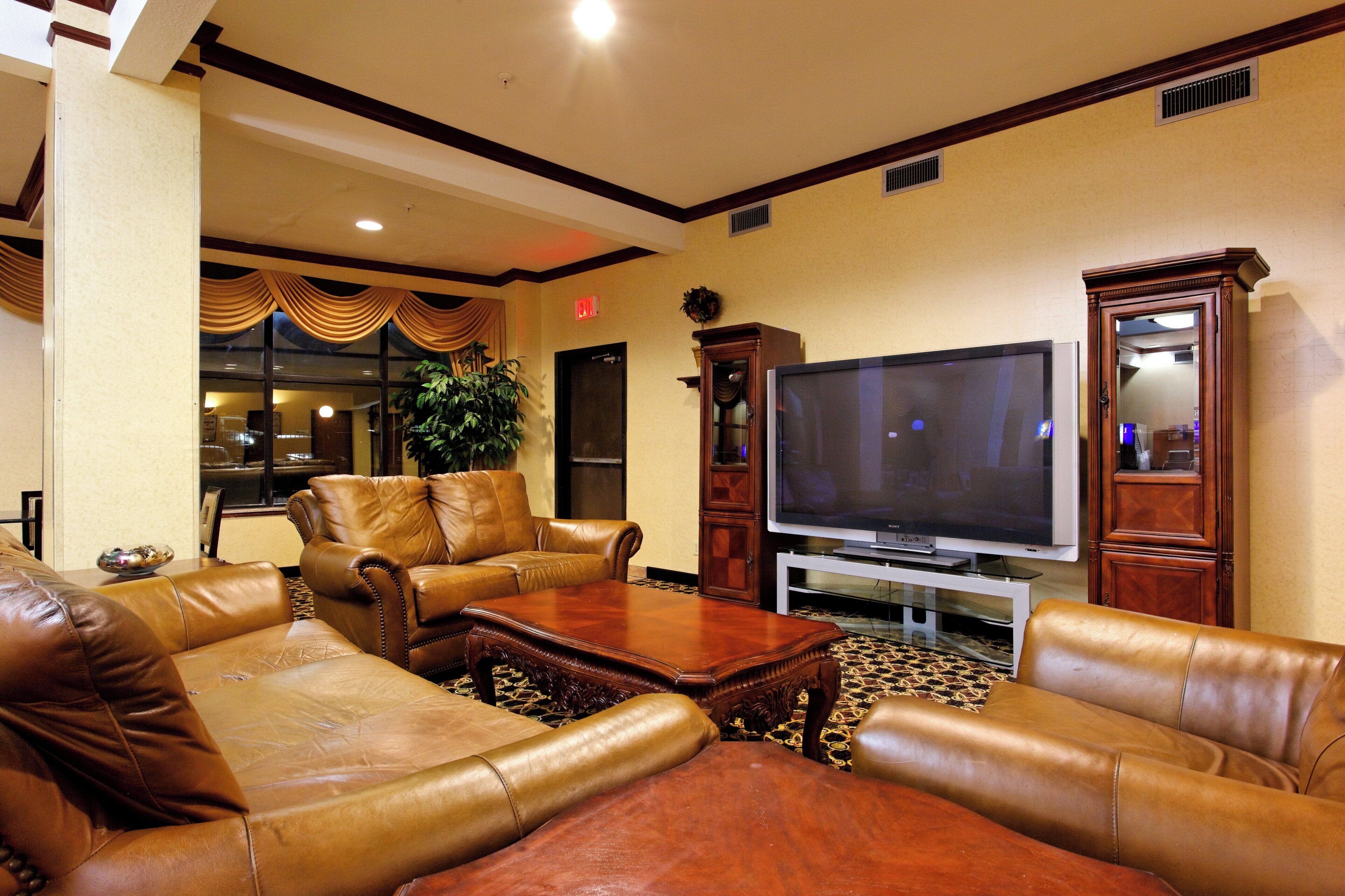 A hotel lobby with leather sofas, a large flat-screen TV, and a patterned carpet.