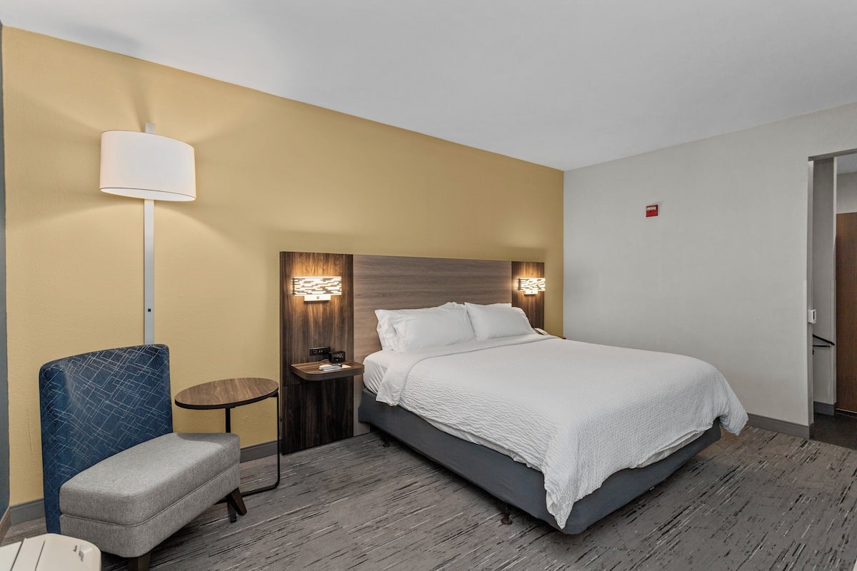 Une chambre d’hôtel comprenant un lit, une chaise, une table de chevet, une lampe et un luminaire fixé au mur.