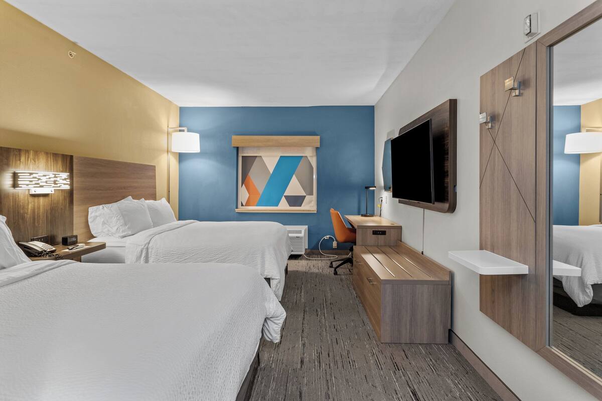 Une chambre d’hôtel avec deux lits, un bureau, une télévision et un grand miroir.