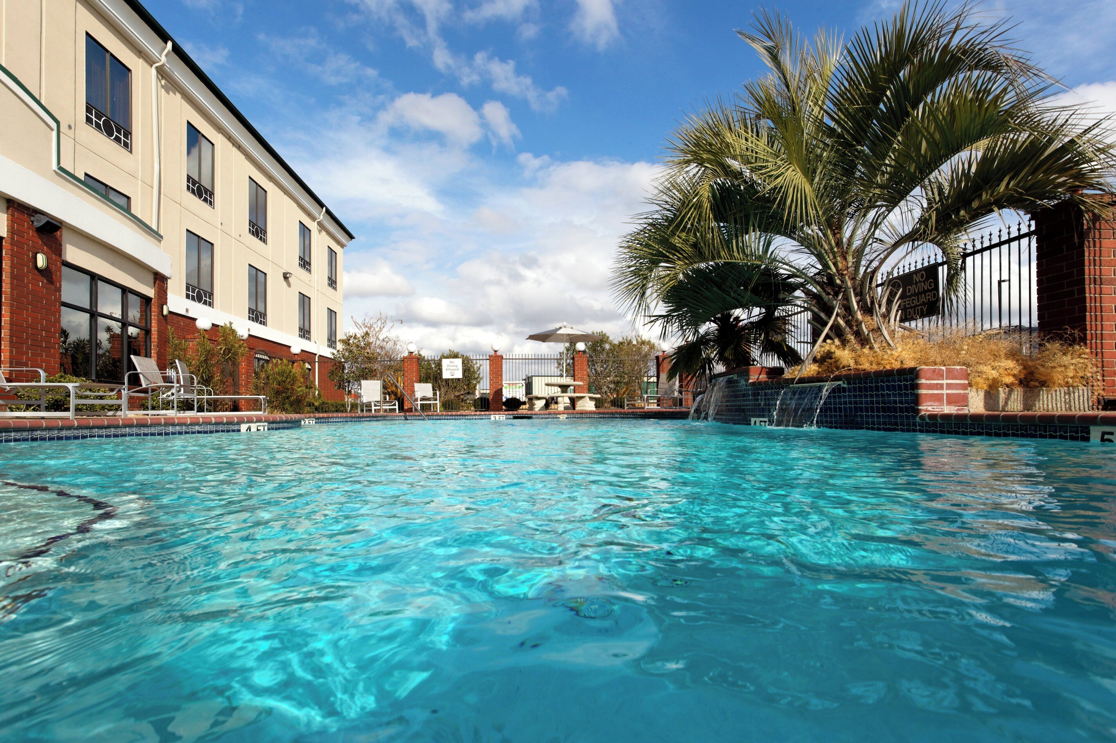 A clear swimming pool with a view of a building and palm trees.