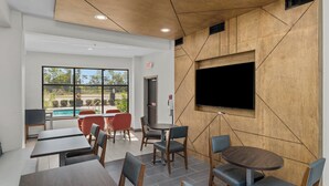 A modern indoor dining area with tables and chairs, a flat-screen TV mounted on the wall, and a view of the outdoors through large windows. - Holiday Inn Express Crockett by IHG (Crockett)