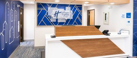 Un comptoir d’accueil agrémenté d’un motif géométrique bleu et blanc sur le mur, d’un panneau décoratif en bois et d’une enseigne indiquant « Holiday Inn Express & Suites ».