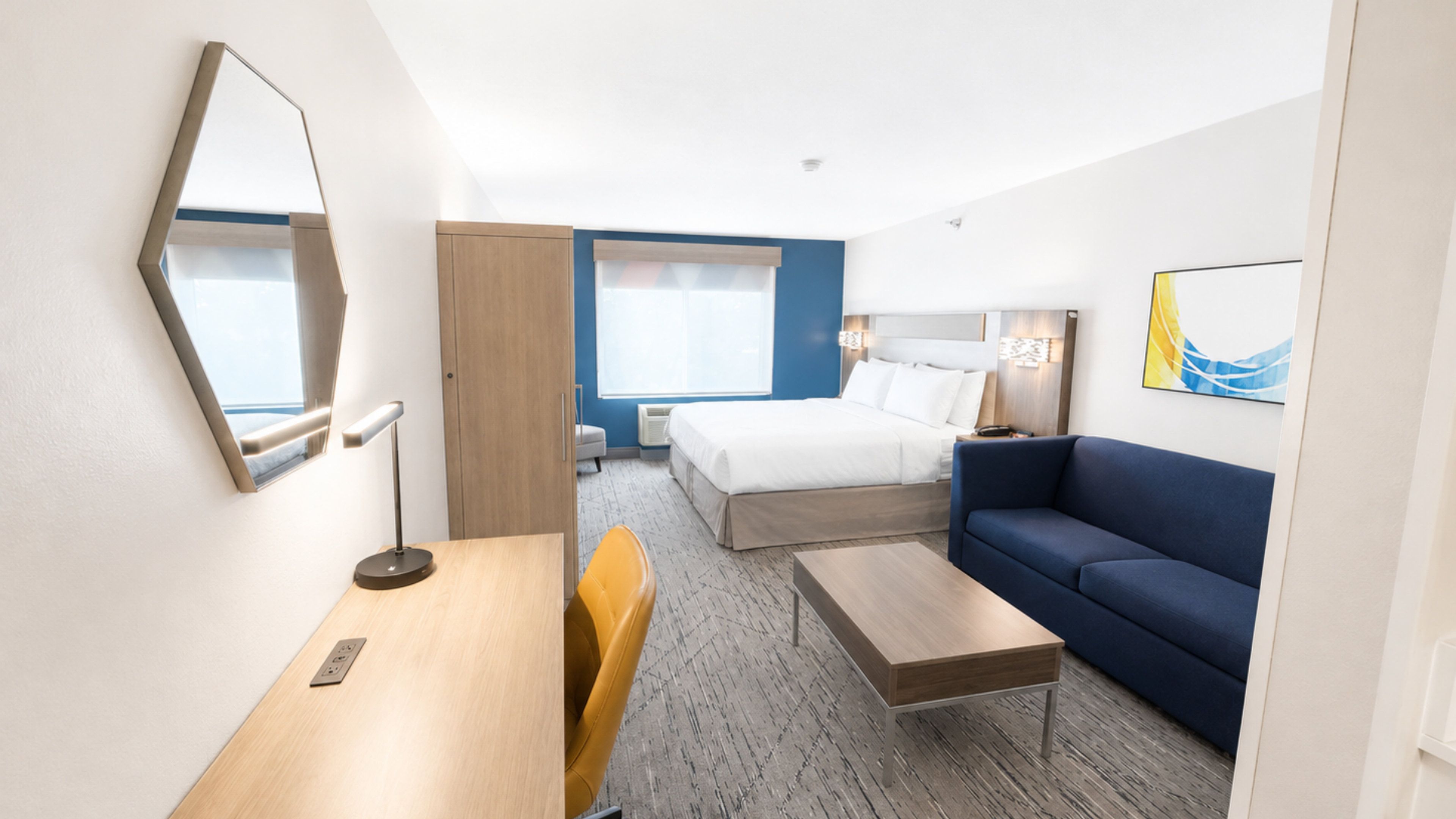 A hotel room with a bed, a desk, a chair, a sofa, and a large mirror.