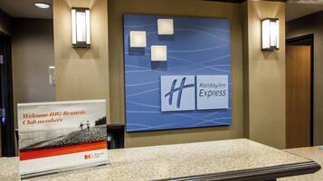 Un área de recepción con un cartel que da la bienvenida a los miembros de IHG Rewards Club, el logotipo de Holiday Inn Express y una lámpara fijada a la pared.