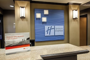 Un área de recepción con un cartel que da la bienvenida a los miembros de IHG Rewards Club, el logotipo de Holiday Inn Express y una lámpara fijada a la pared.