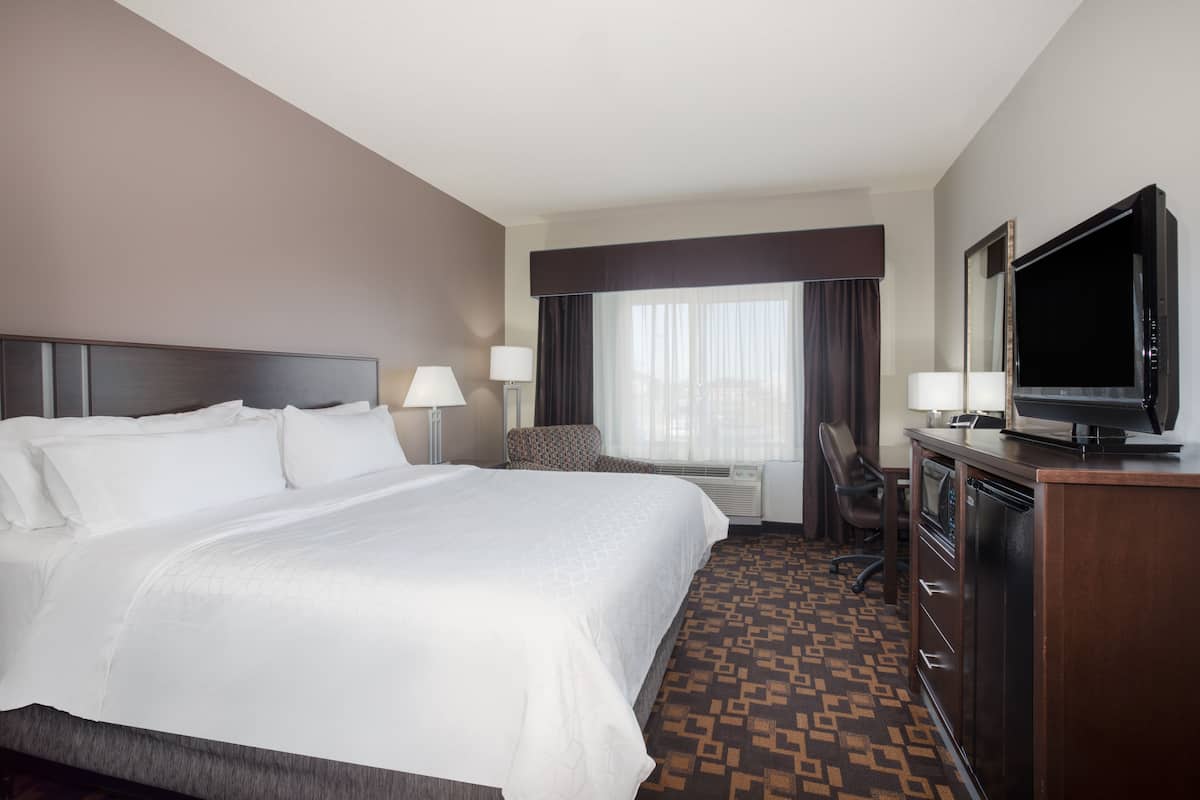 A hotel room with a large bed, a desk with a television, a chair, and a window with curtains.