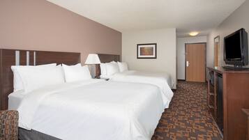 Habitación de hotel con dos camas, un escritorio, un televisor y una alfombra estampada.